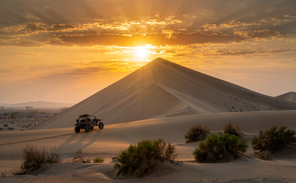 Camel caravan walking across tall golden sand dunes in Badain Jaran Desert