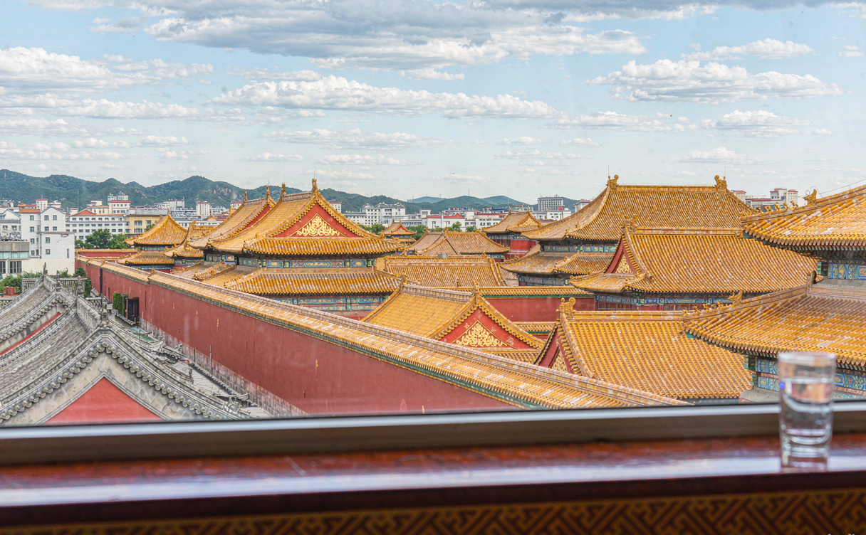 Hotel room window view over the Forbidden City's golden rooftops at dusk