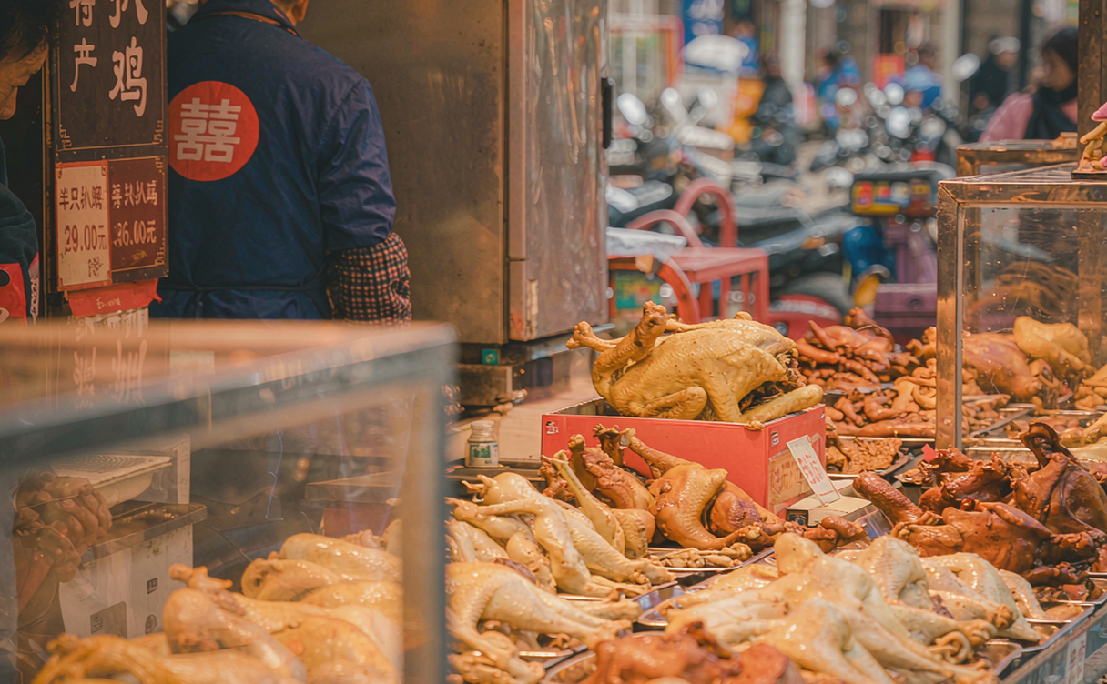 A Dezhou braised chicken market stall with hanging poultry and displays of aromatic spices