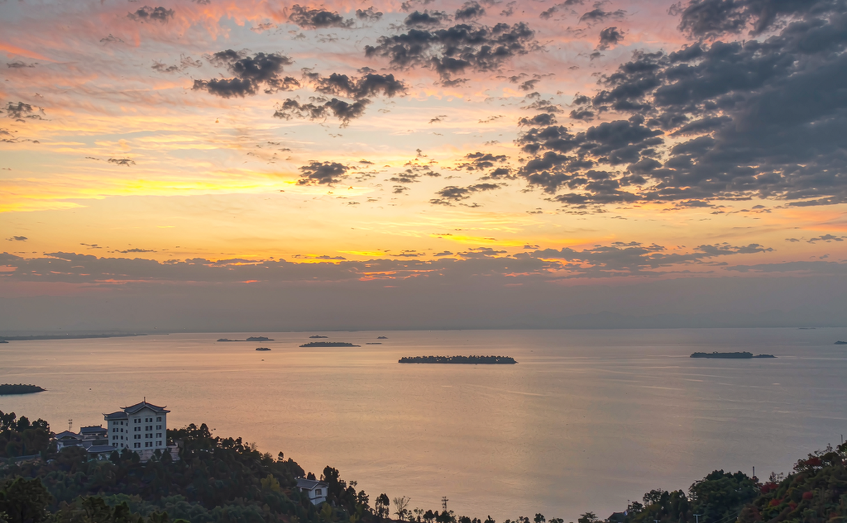 Sunset over Fuxian Lake in Yunnan with orange clouds reflected on calm water and hills on the horizon