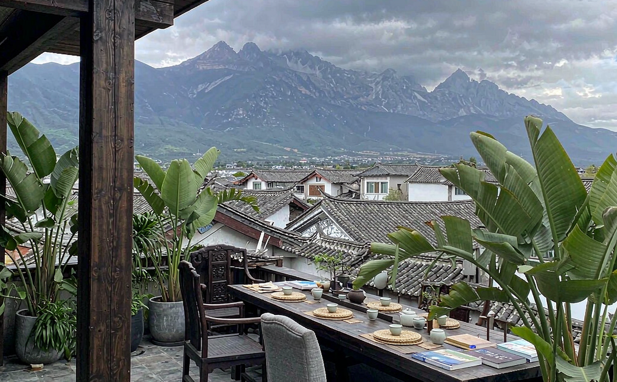 A boutique inn rooftop terrace overlooking Lijiang old town grey tiles with Jade Dragon Snow Mountain in the distance