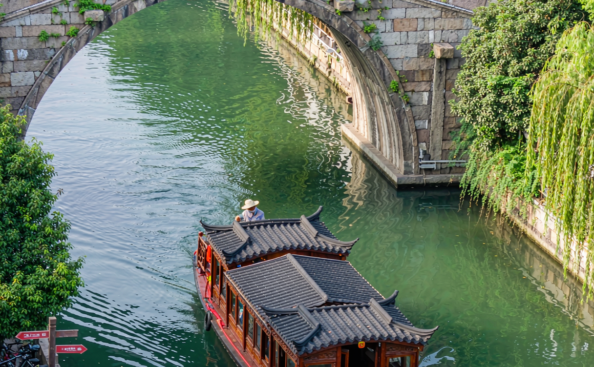 Wooden canal boat passing under an arched stone bridge in Luzhi water town, Jiangsu