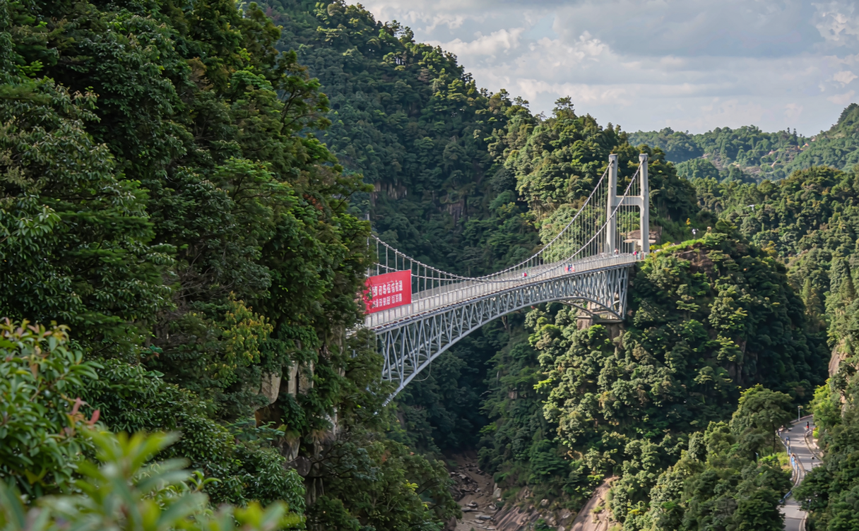 Glass skywalk edge with visitors looking out over a misty Mangshan forest gorge in Hunan