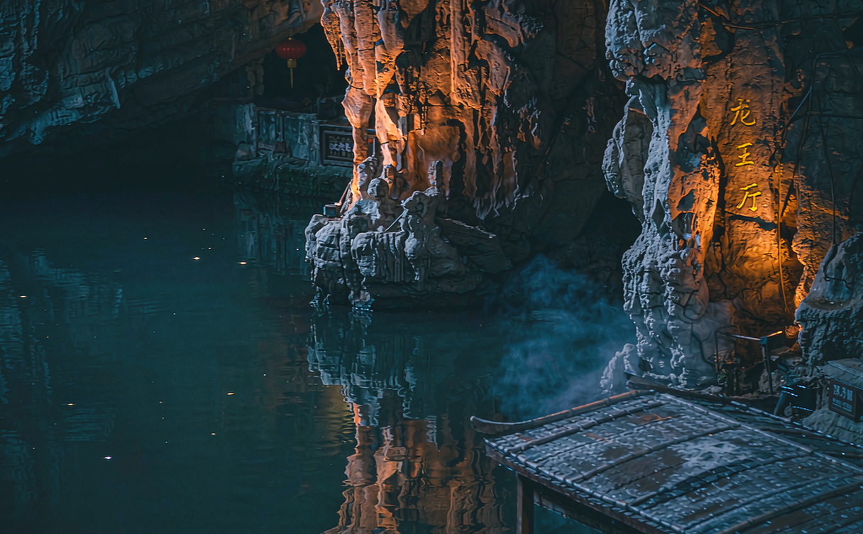 A small boat passing under lit stalactite formations inside Shuanglong Cave in Jinhua, Zhejiang