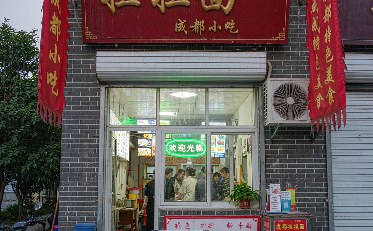 A Chengdu night snack stall with bowls of dan dan noodles and skewers under warm lights