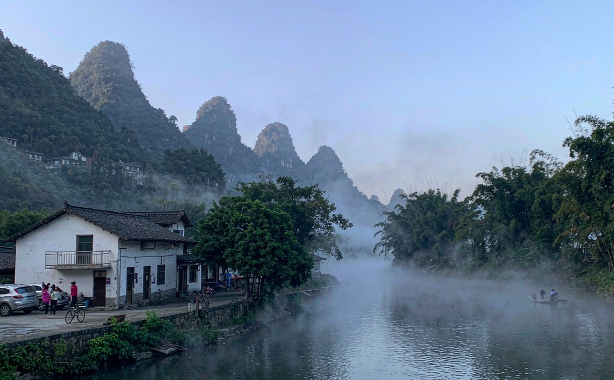 A bamboo raft on the Yulong River near Yangshuo passing an old stone bridge with karst peaks in the background