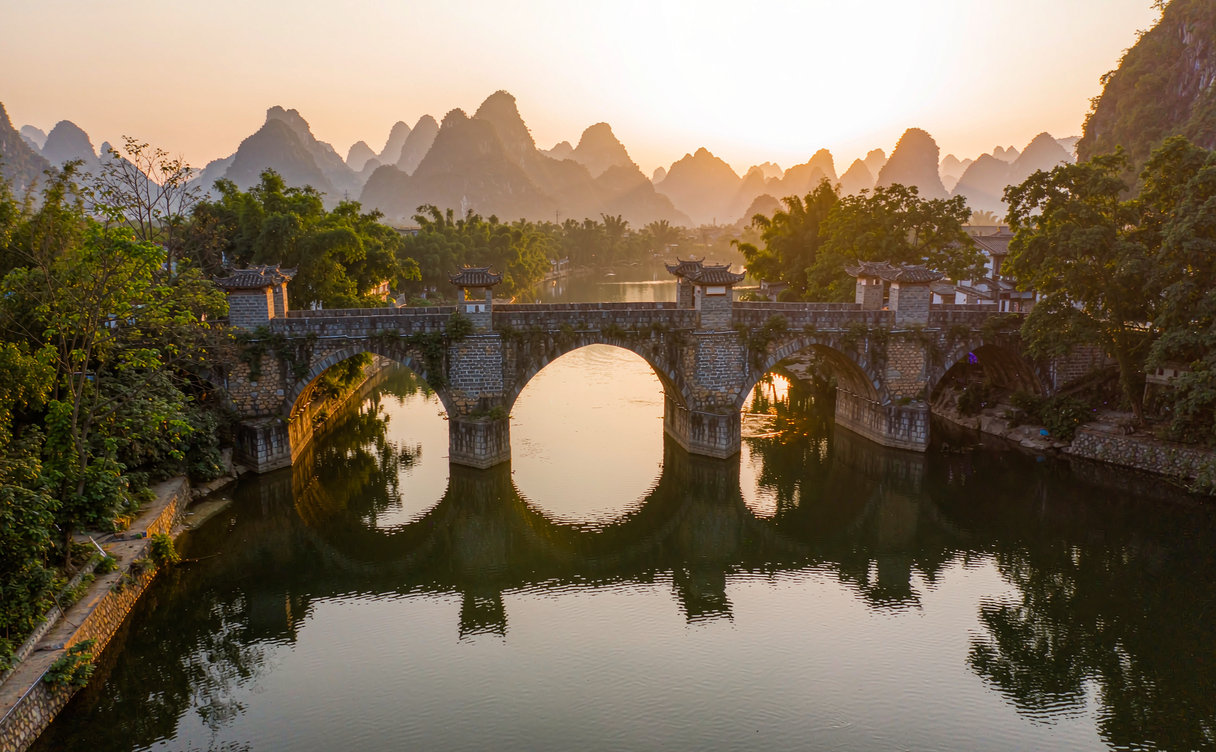 Bamboo raft floating under an old stone arch bridge on the Yulong River near Yangshuo
