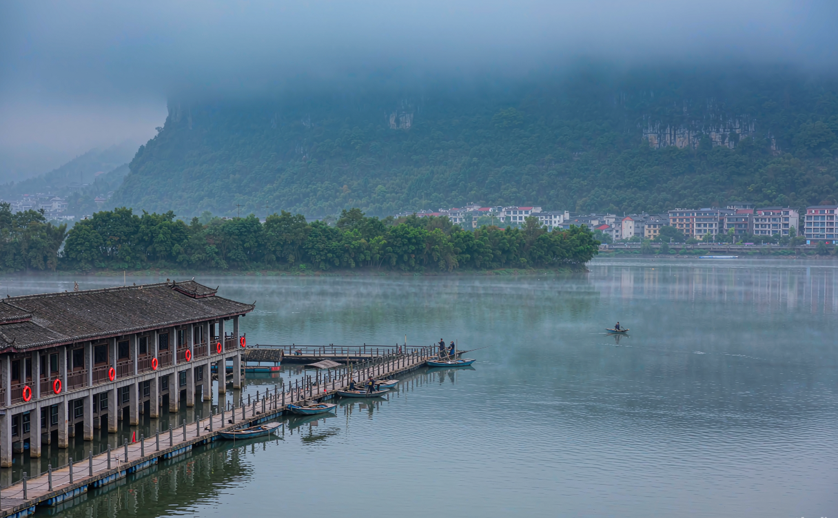 A quiet south-bank balcony room overlooking the lit rooftops and river of Fenghuang at dusk