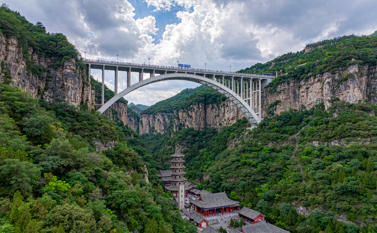 Stone arch bridge spanning the canyon with the mountain temple pavilion of Cangyan Mountain
