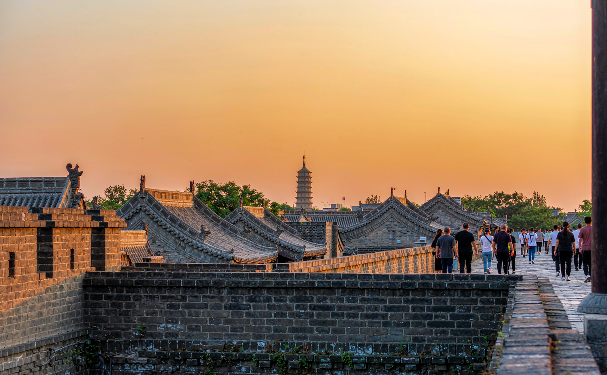 Visitors on a Chinese city wall at sunset with historic rooftops