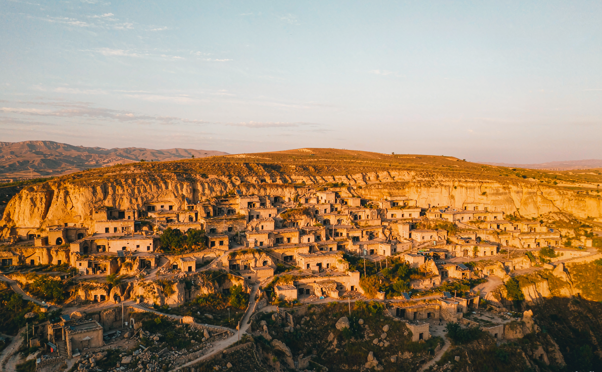 A Loess Plateau yaodong cave courtyard at sunset with chimneys and a stone mill