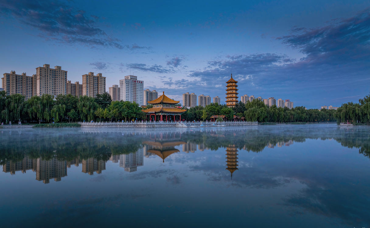 Jinan city skyline reflected in the still water of Daming Lake at dusk