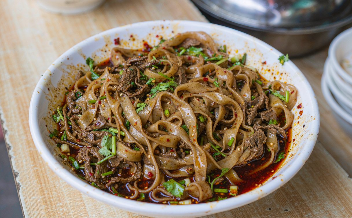 A wooden counter bowl of Henan braised hui mian noodles with lamb slices and fresh coriander