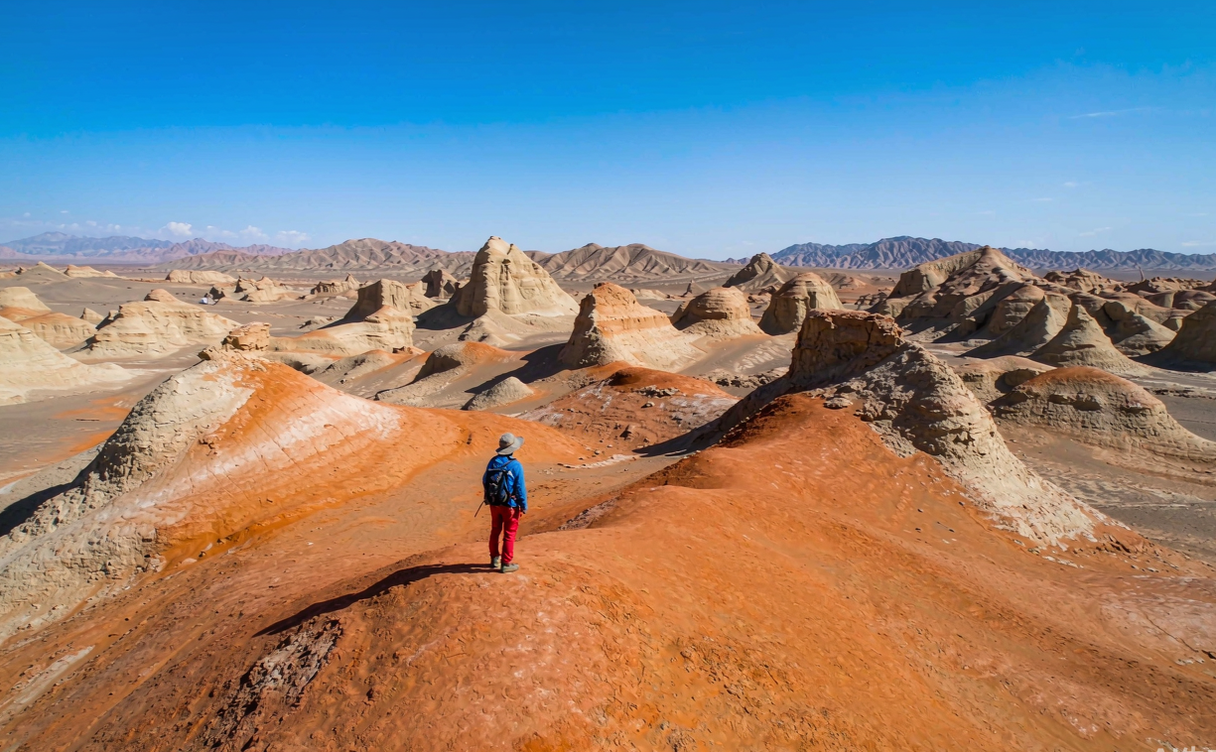 A lone traveler standing on the orange-red Yardang desert landscape near Mangnai, Qinghai, China