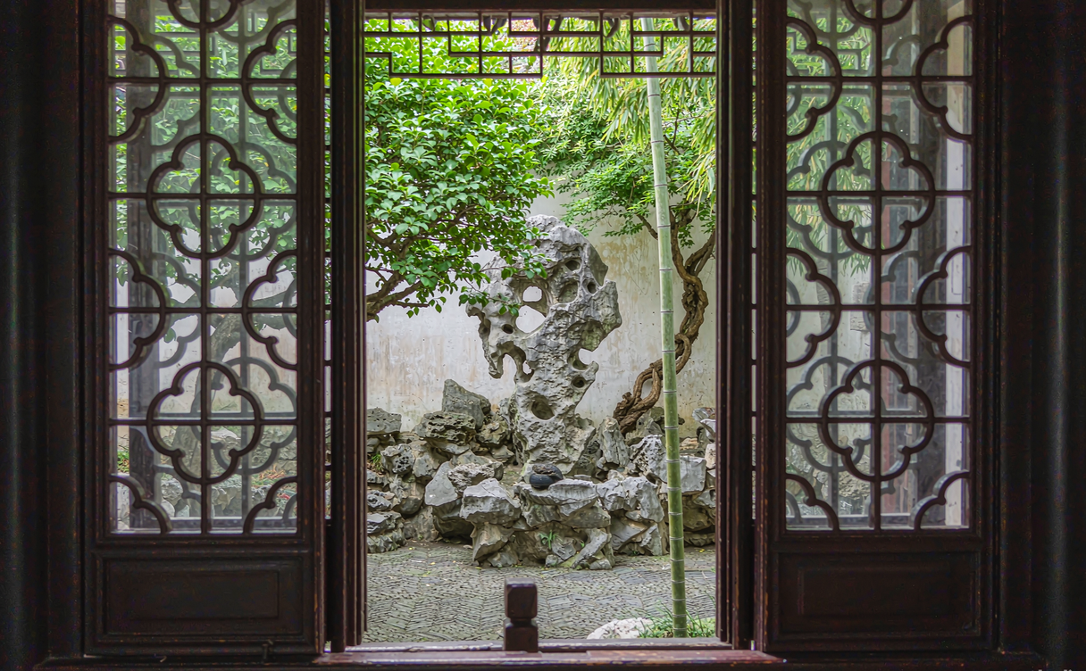 Ornate lattice window framing a miniature rockery in the Master of the Nets Garden
