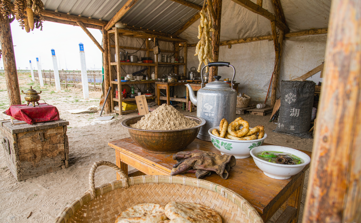 A wooden table spread of hand-pulled lamb ribs, yak yoghurt in a clay bowl and plateau flatbread in Qinghai
