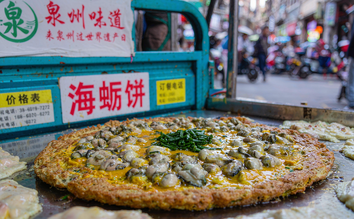 An oyster omelette frying on a flat iron griddle at a Quanzhou street food stall