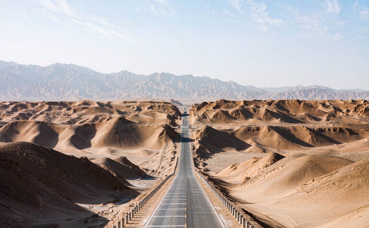 Straight desert highway crossing Taklimakan dunes under big sky