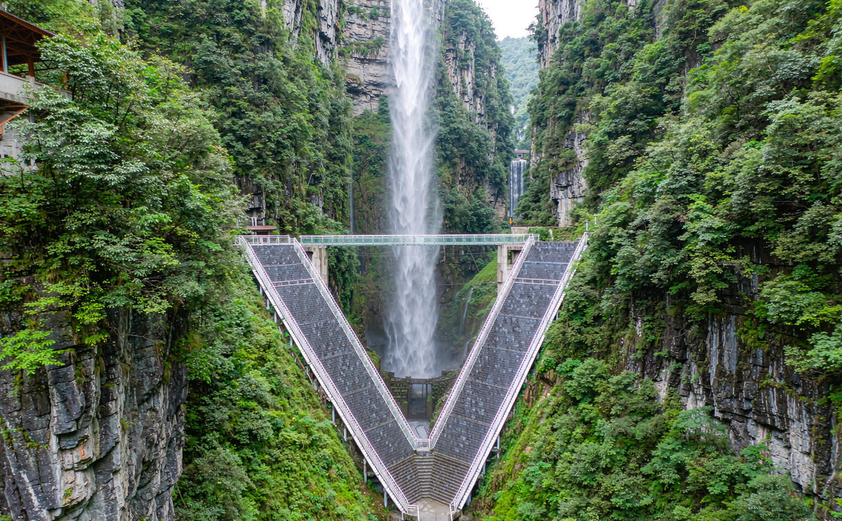 Visitors crossing the long transparent glass deck of the Zhangjiajie Grand Canyon bridge above a deep green valley in Hunan, China