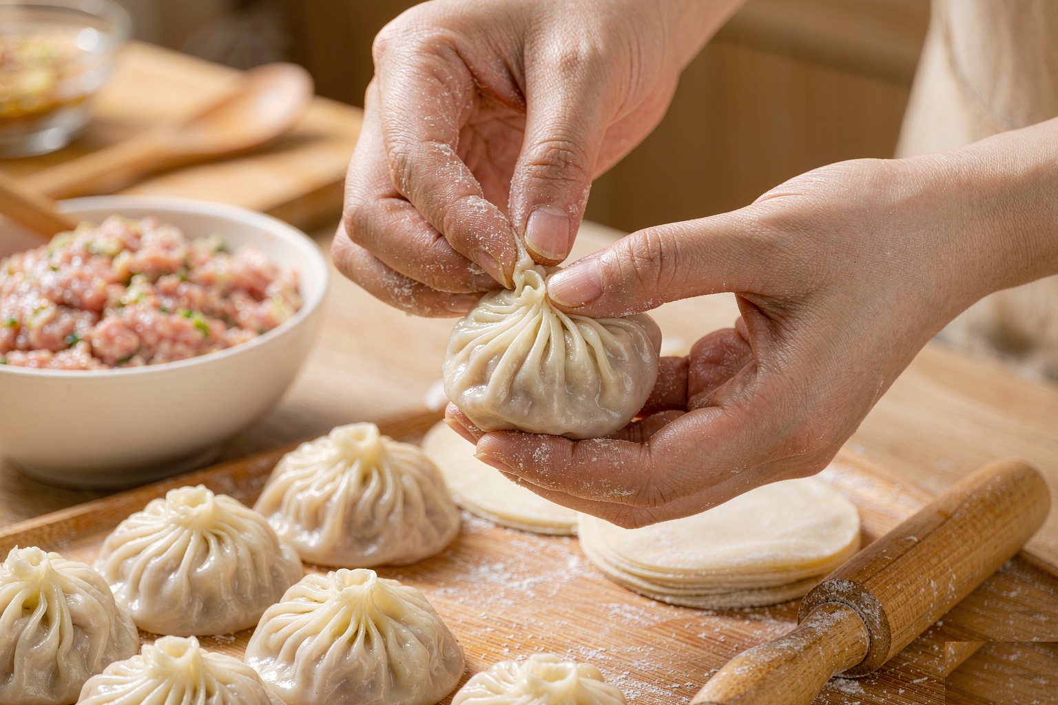 Hands pleating a xiaolongbao wrapper filled with pork and aspic