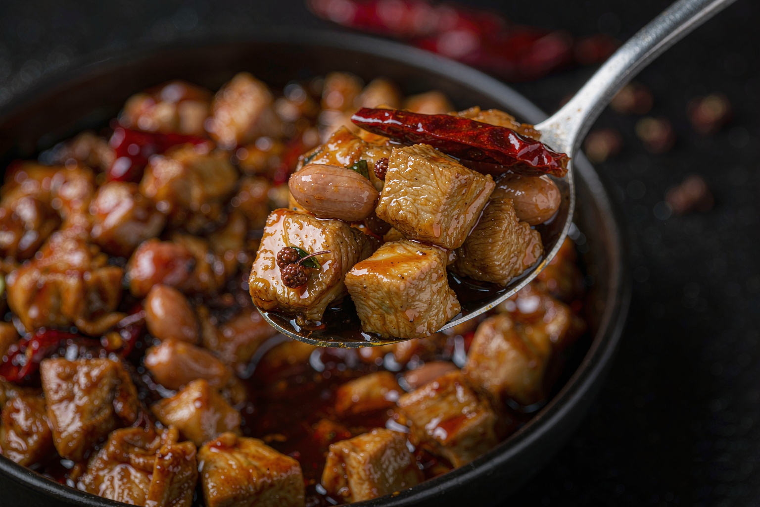 Close-up of kung pao chicken with glossy sauce, peanuts and a dried chili