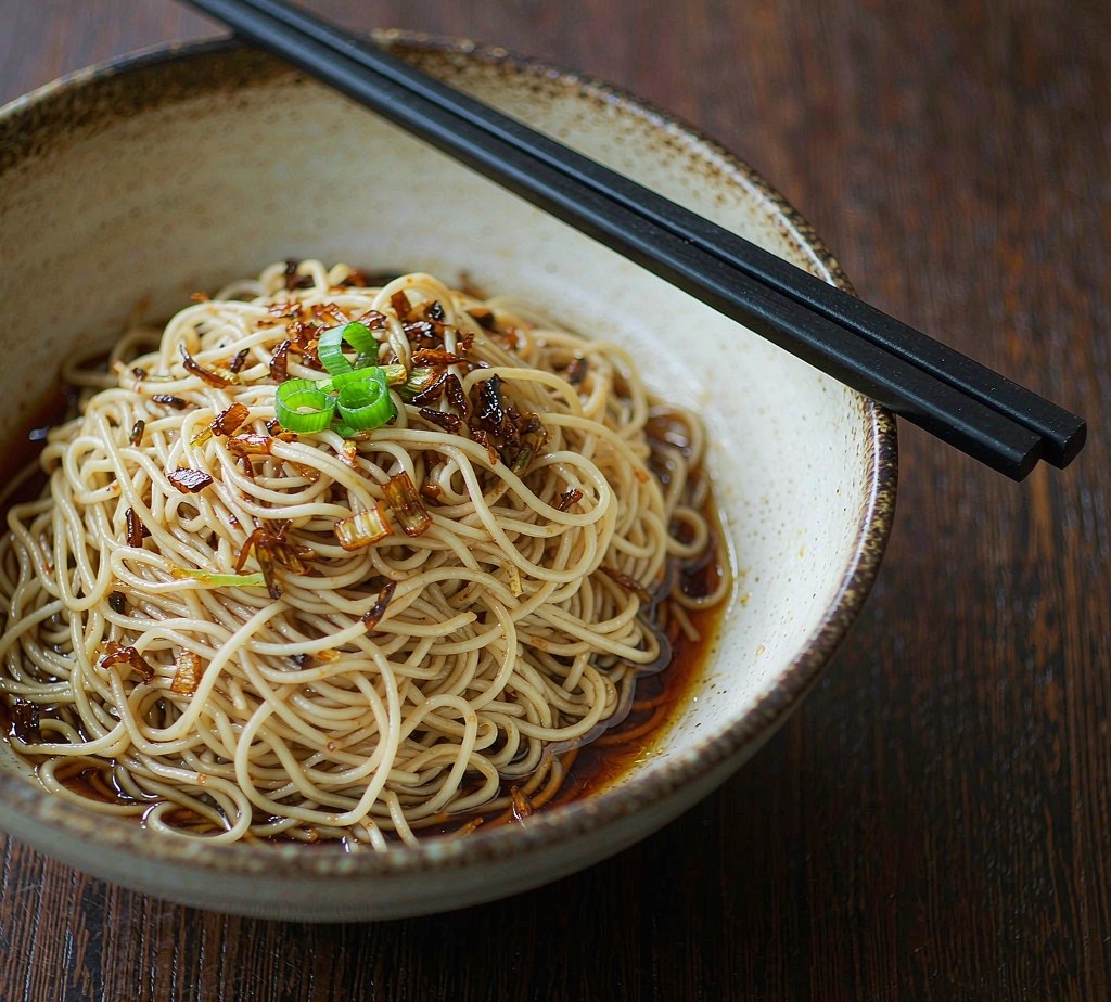 Bowl of Shanghai scallion oil noodles with crispy fried scallions and dark soy sauce, chopsticks resting on the rim