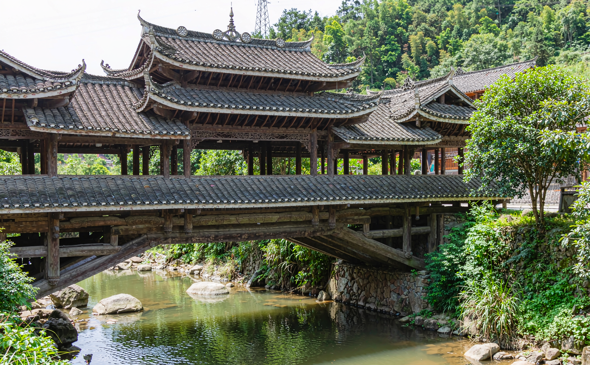An ornate wooden covered bridge over a green stream in Taishun, Zhejiang, China