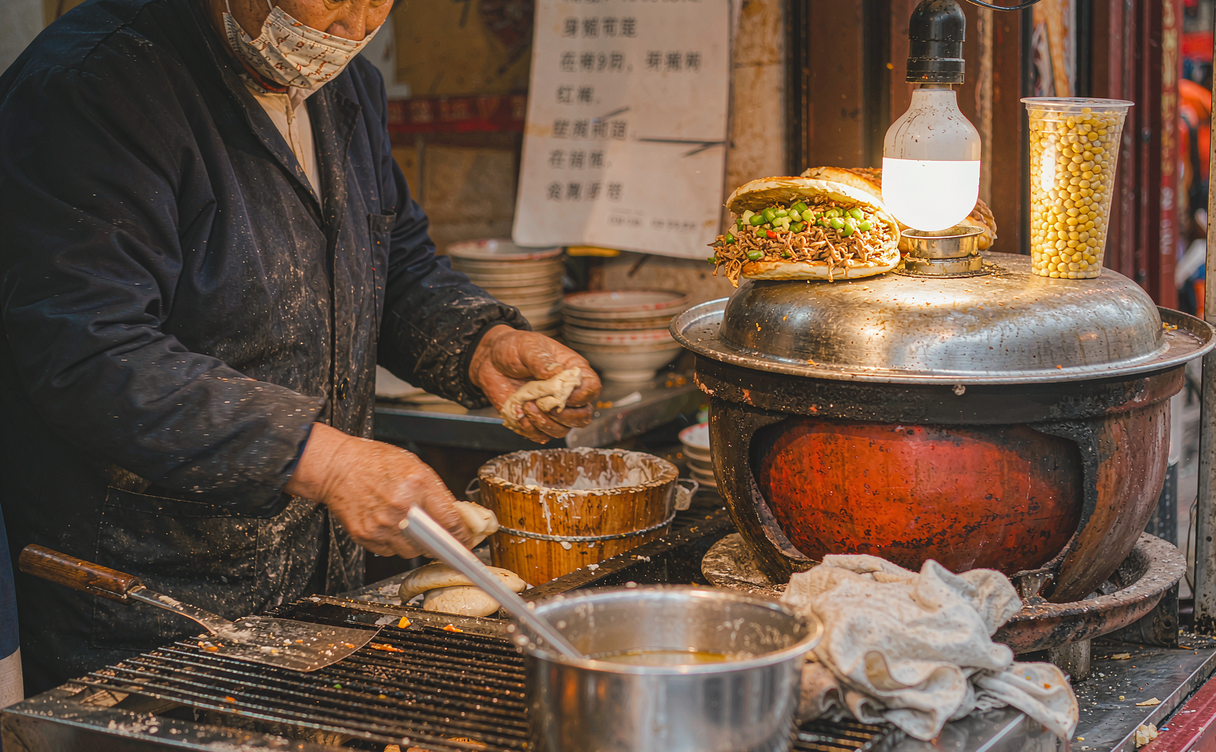 Xi'an night market stall grilling roujiamo baijimo buns over charcoal